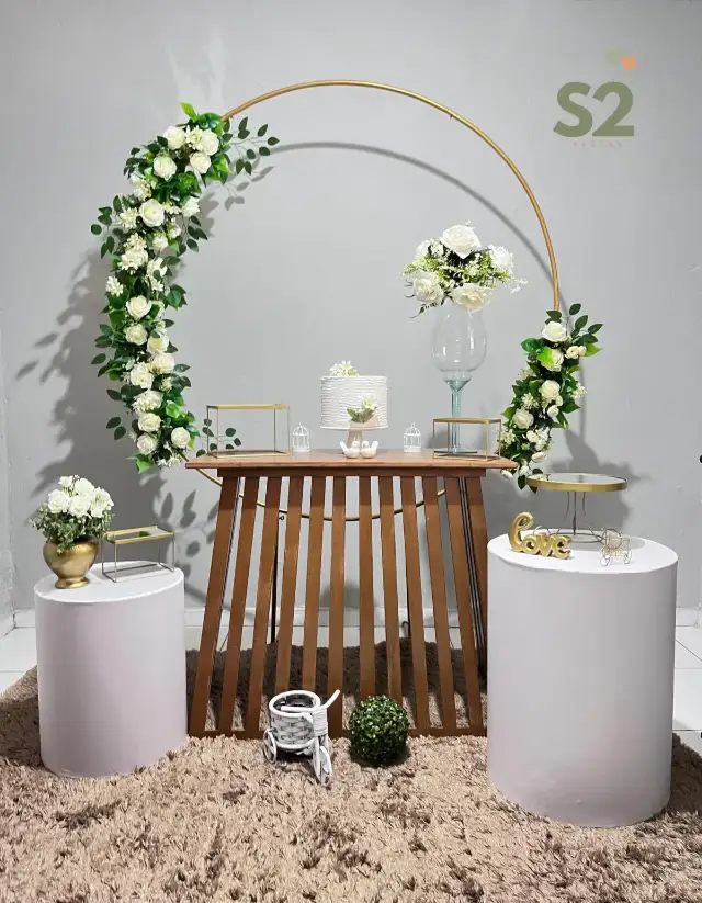 Arco dourado com flores sobre mesa de madeira e cilindros brancos