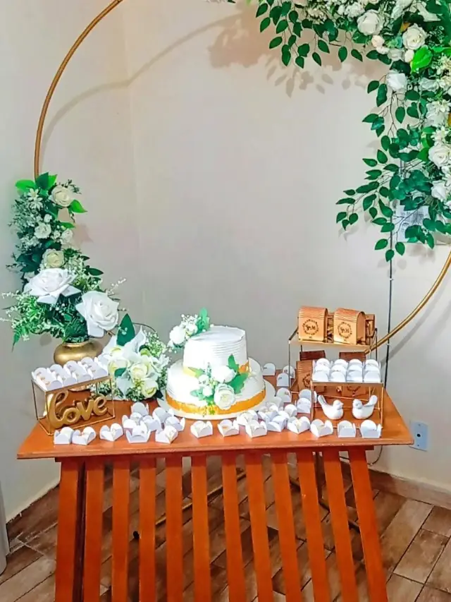 Casamento intimista com arco dourado de flores e mesa de madeira com bolo e doces