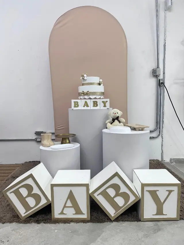 Chá de bebê com painel em arco bege, cubos BABY e bolo de dois andares