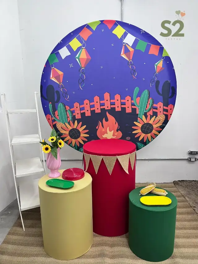 Decoração de festa junina com painel redondo, cilindros coloridos e bandejas